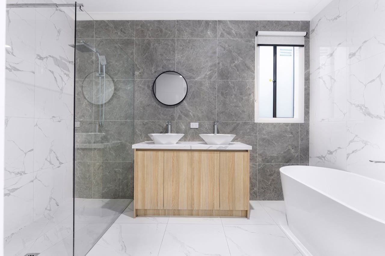 A sleek and stylish modern bathroom with minimalist design, featuring dual washbasins, marble tiles, and a glass shower enclosure.